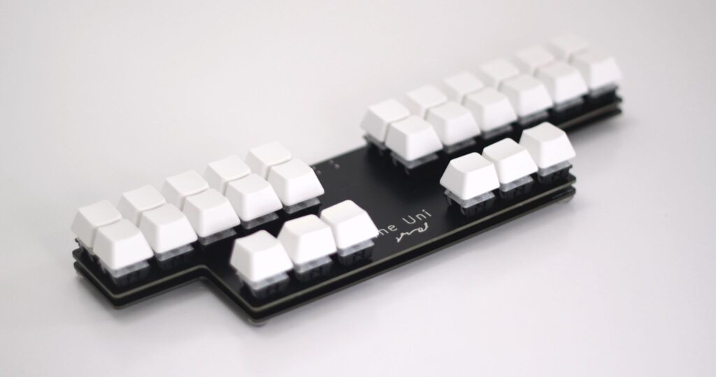 A modern steno keyboard, called the Uni. Black plastic with three rows of white keyboards, unmarked and broken into two sections.