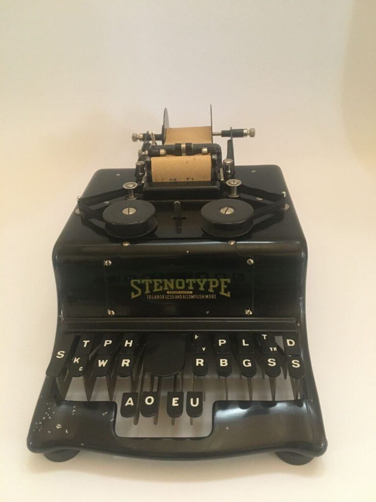A Stentoype machine, black finish. The keyboard has far fewer keys than a conventional alphanumeric keyboard: a few letters and specialized keys, black plastic with white writing on them.