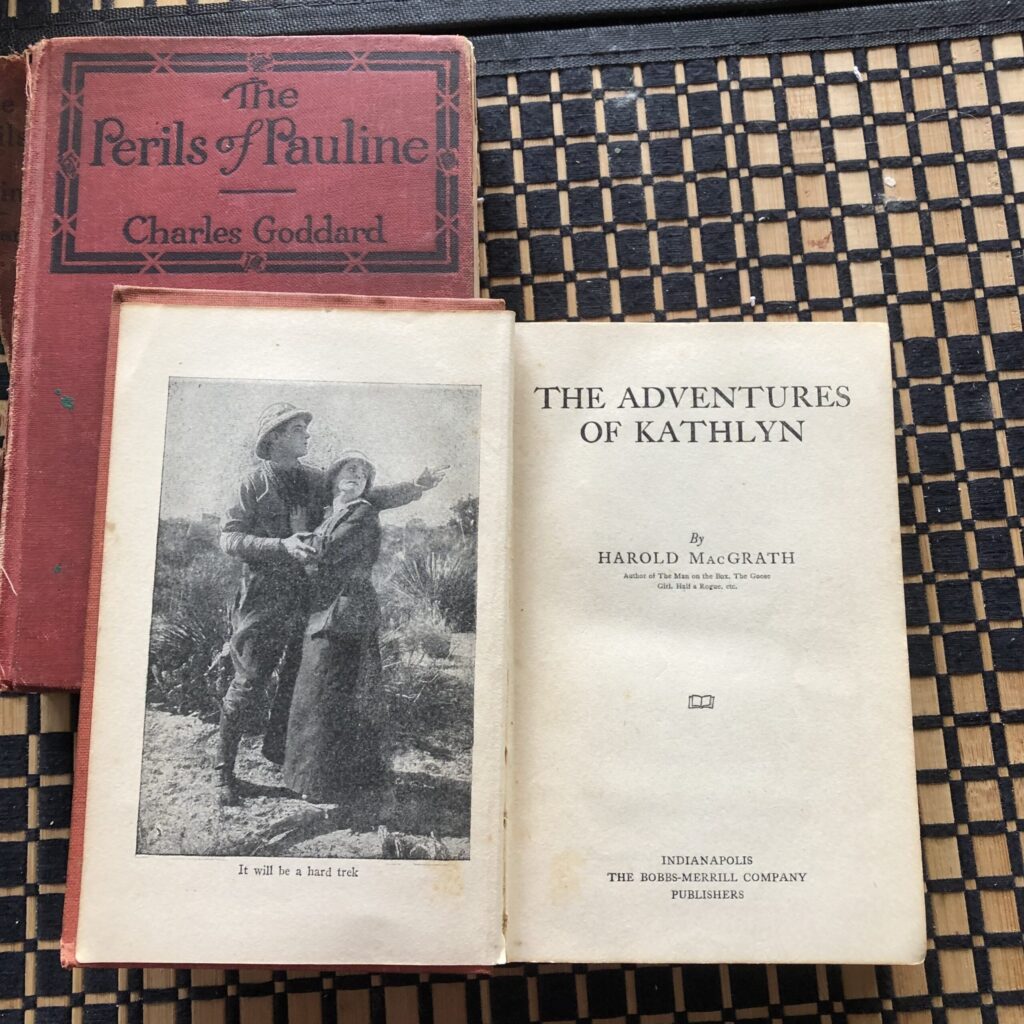 Two stacked books, one closed (red cover), one opened at title page.