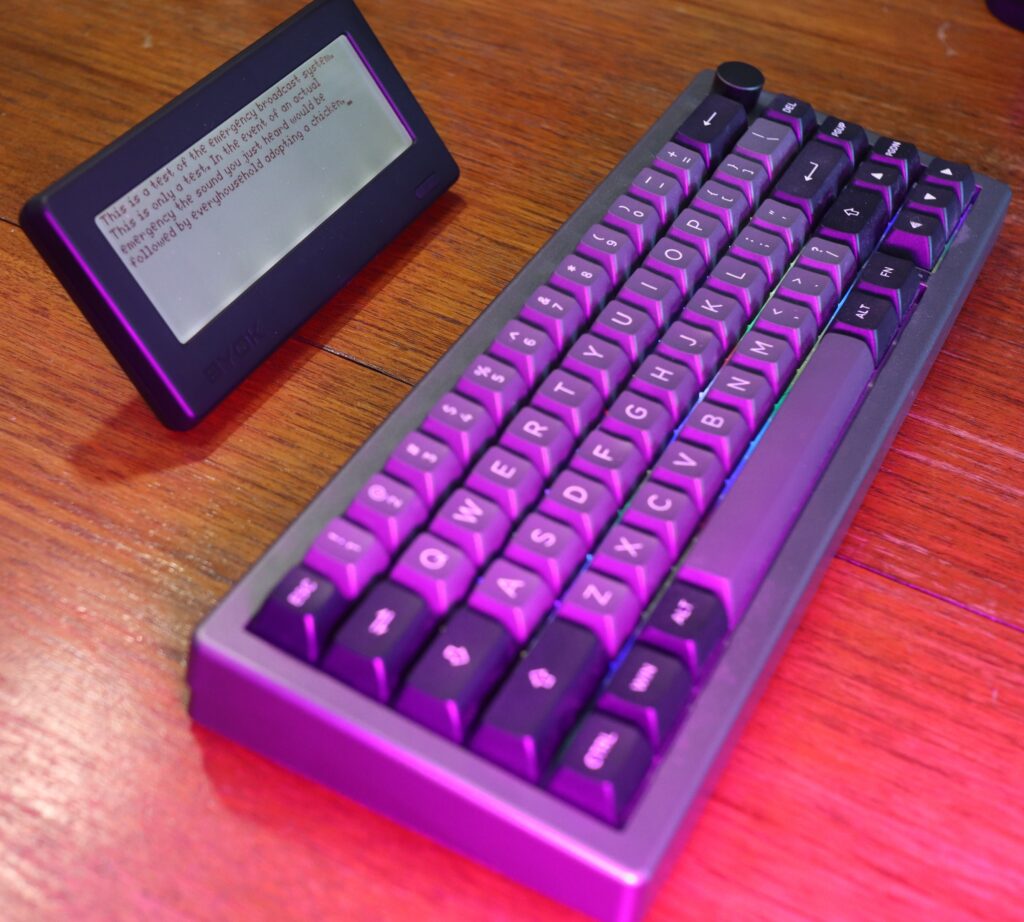 A writer deck (rectangular device with a white screen) paired with a QWERTY keyboard on a desk.